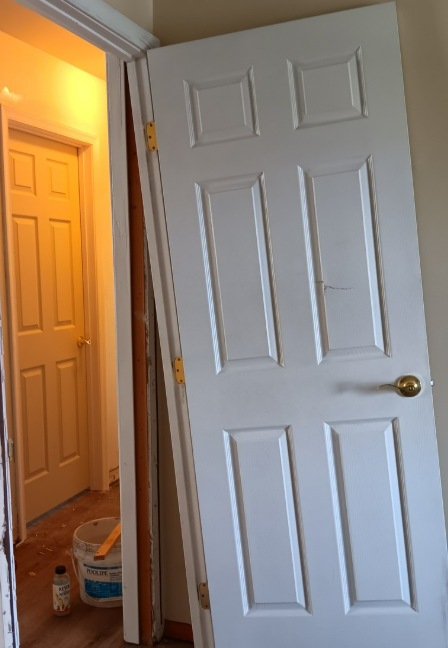 White six-panel door propped open next to doorway, a second door visible down a hallway.