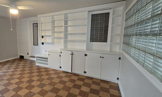 Room with built-in white shelves and cabinets. Checkered floor and a glass block wall.