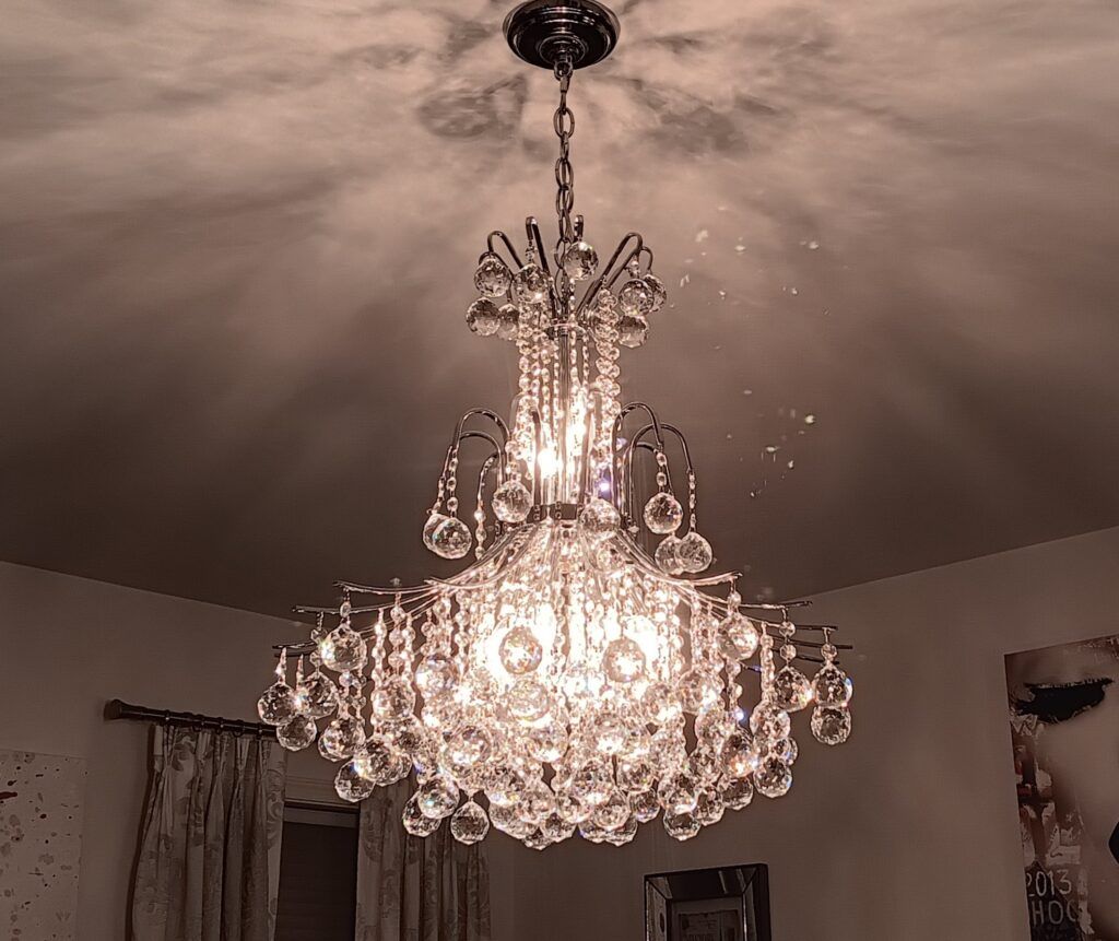 Crystal chandelier hangs from a ceiling, reflecting light and casting shadows in a room.